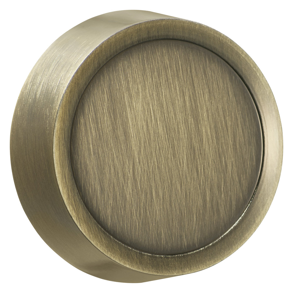 Close-up view of an antique brass dimmer knob with a vintage, weathered appearance. The knob features a smooth, rounded surface with subtle patina, giving it a classic, antique feel. The knob is mounted on a wall, with a slender metal shaft visible behind it.