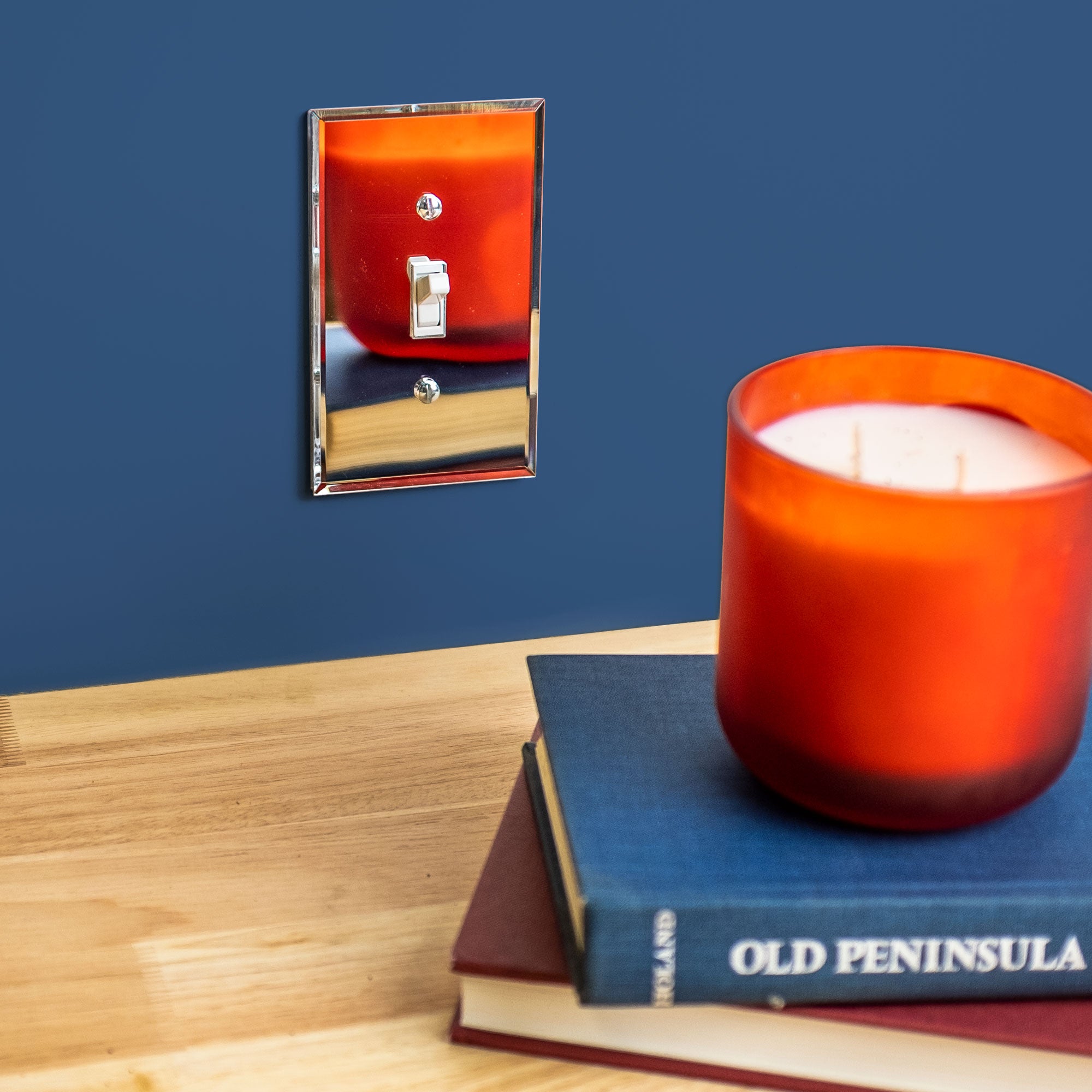 Reflective light switch cover with a sleek, polished finish, adding a modern and stylish touch to any space, showing off its reflective nature through the mirror image of a amber colored candle.