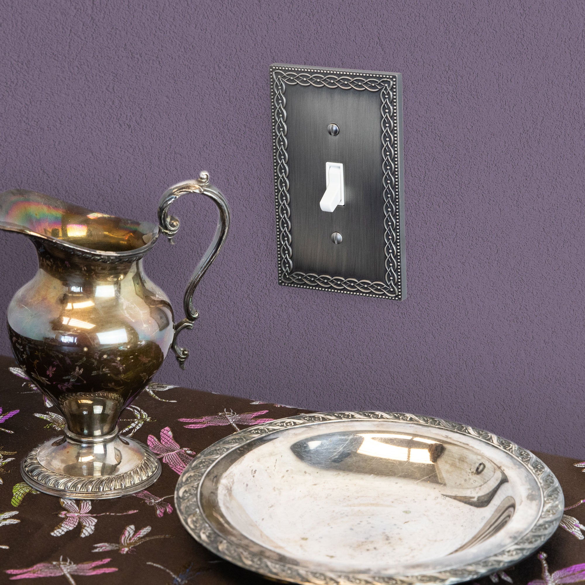 Antique nickel light switch cover featuring a brushed metallic finish with a vintage, decorative design, adding an elegant, timeless touch to the space against a purple wall.